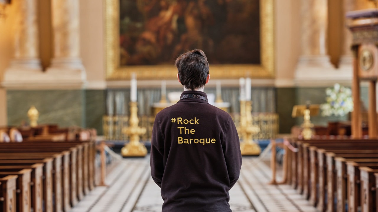 Team member standing in Chapel. His jumper says 'Rock the Baroque'